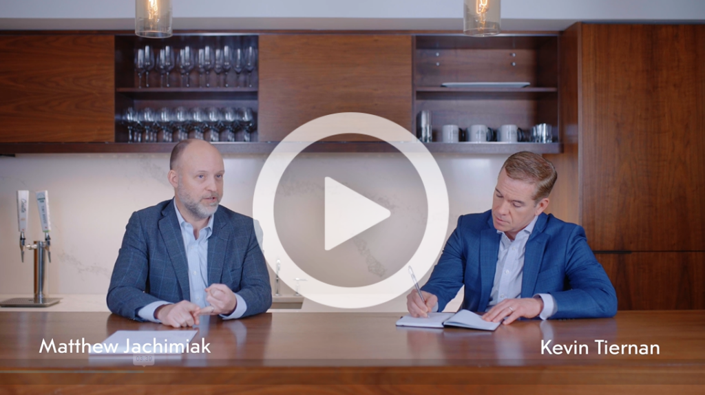 Two professionals in a business meeting, video play button overlay.